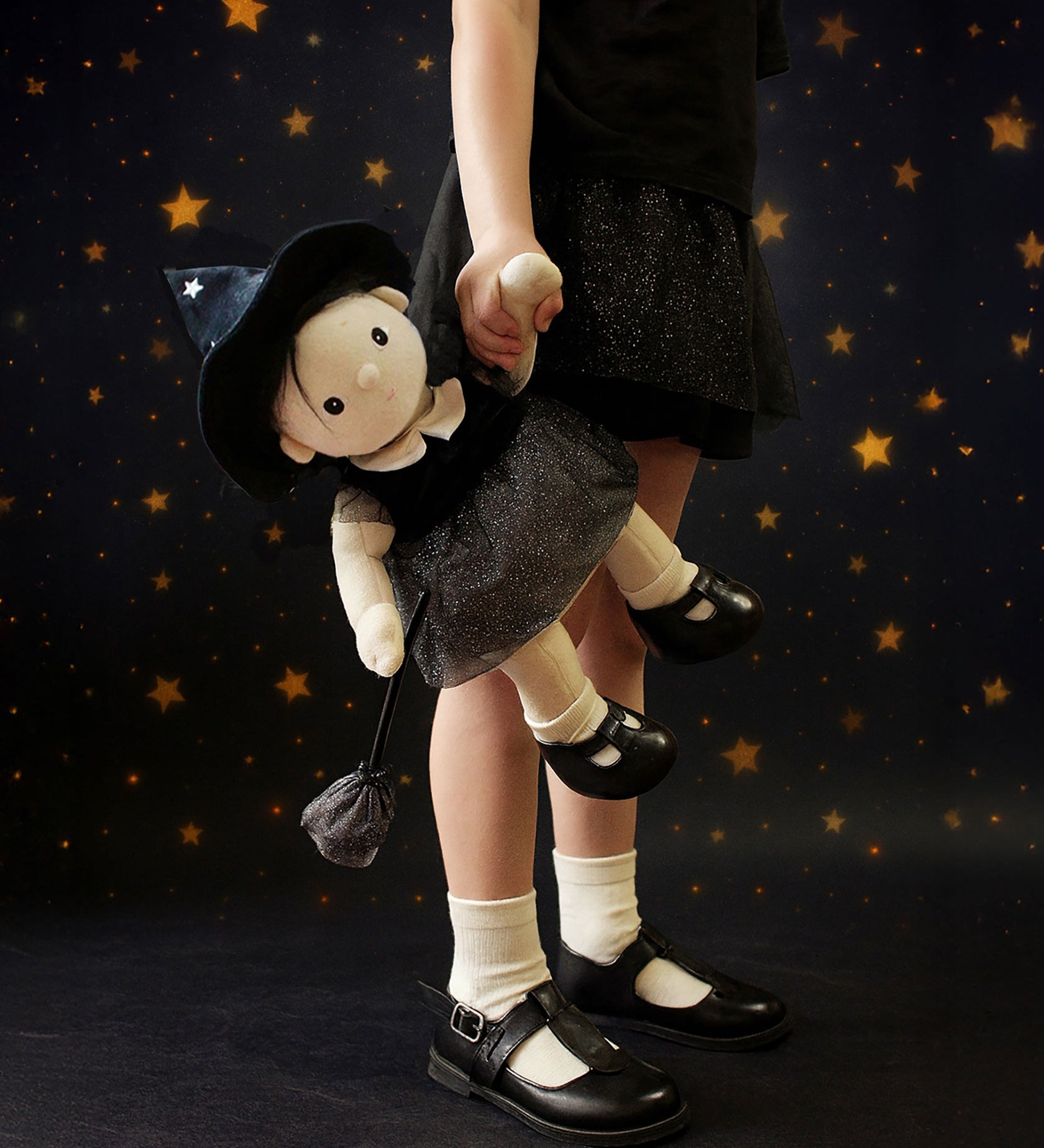 A child carrying the Olli Ella Wendy Witch dream Dinkum doll by their hand. A dinkum doll with a black dress, witches hat, black shoes and a magnetic broom accessory. This doll is part of Olli Ella's Halloween collection available here at Babipur.