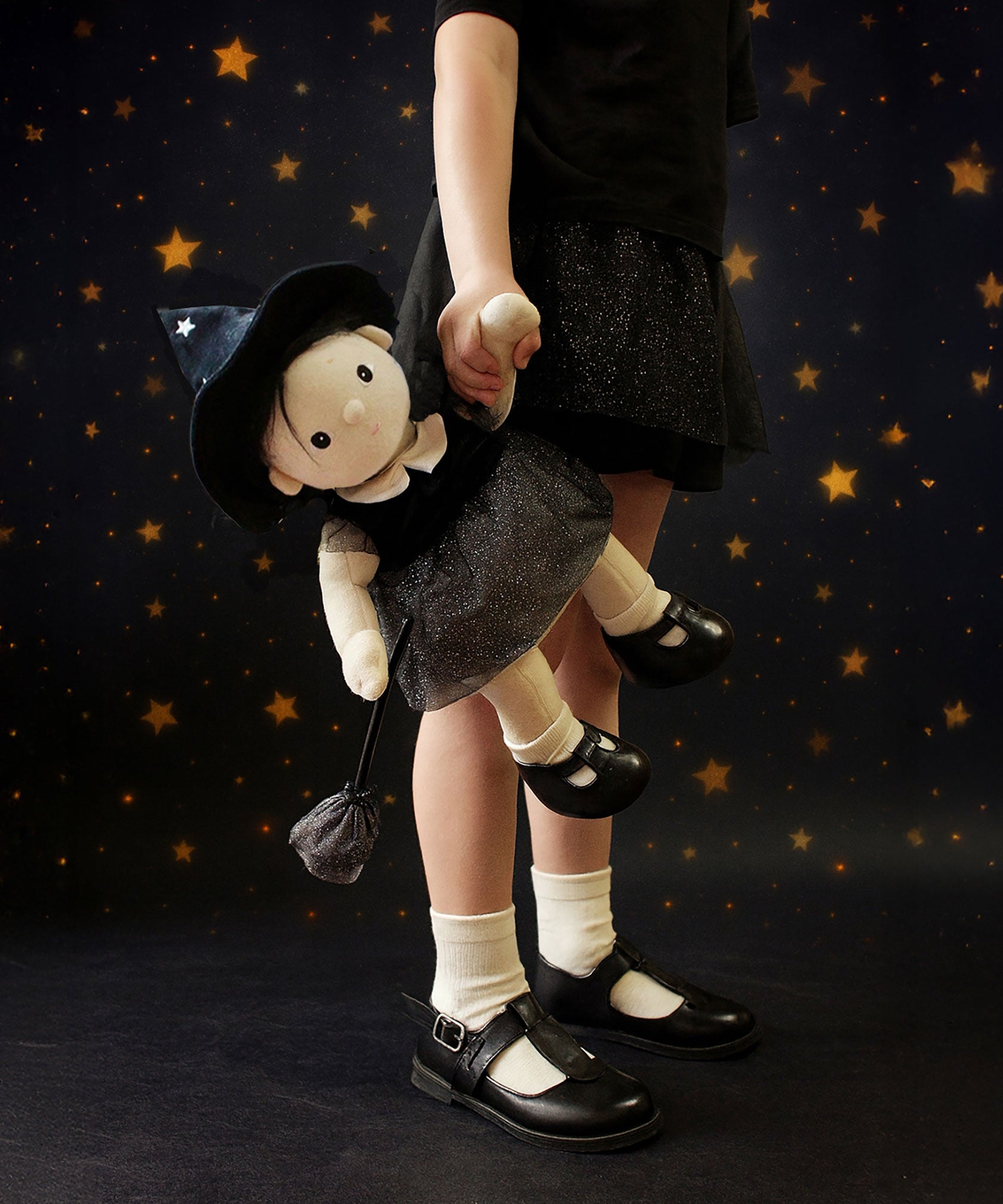 A child carrying the Olli Ella Wendy Witch dream Dinkum doll by their hand. A dinkum doll with a black dress, witches hat, black shoes and a magnetic broom accessory. This doll is part of Olli Ella's Halloween collection available here at Babipur.
