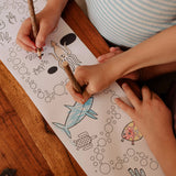 Two children colour in the Olli Ella Playpa Children's Colouring Paper Roll Travel Pack  -  Ocean Design in a home setting.