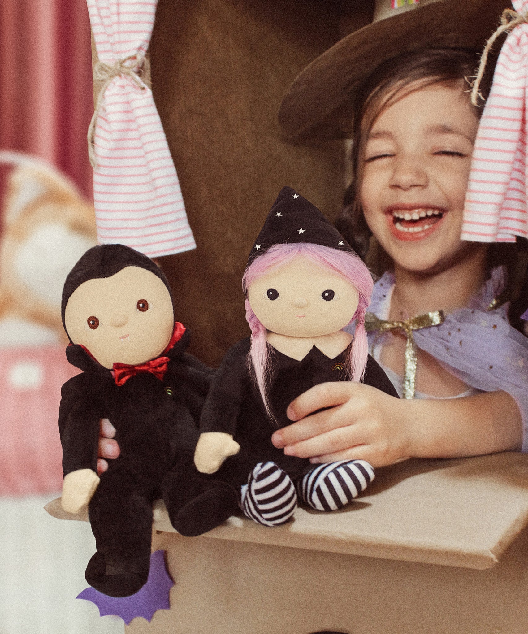 A child playing with a Vincent vampire and a Willa Witch dinky dinkum doll.  These soft toys are part of Olli Ella's Halloween collection available here at Babipur.