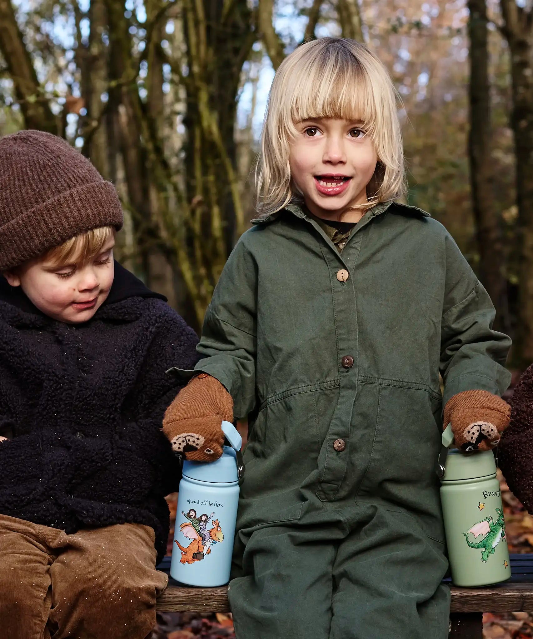 Children sitting on a wooden bench and holding a blue and green Zog One Green Bottle stainless steel bottles