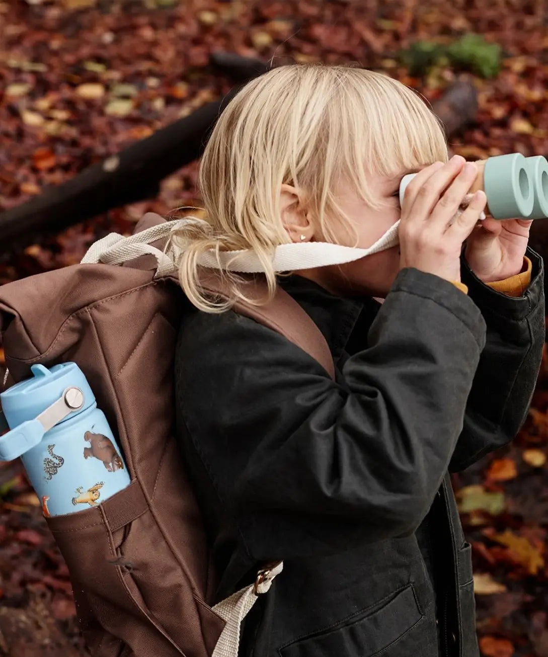 Child in the woods with a One Green Bottle blue with repeating Gruffalo design bottle in a holder on a backpack