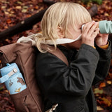 Child in the woods with a One Green Bottle blue with repeating Gruffalo design bottle in a holder on a backpack