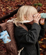 Child in the woods with a One Green Bottle blue with repeating Gruffalo design bottle in a holder on a backpack