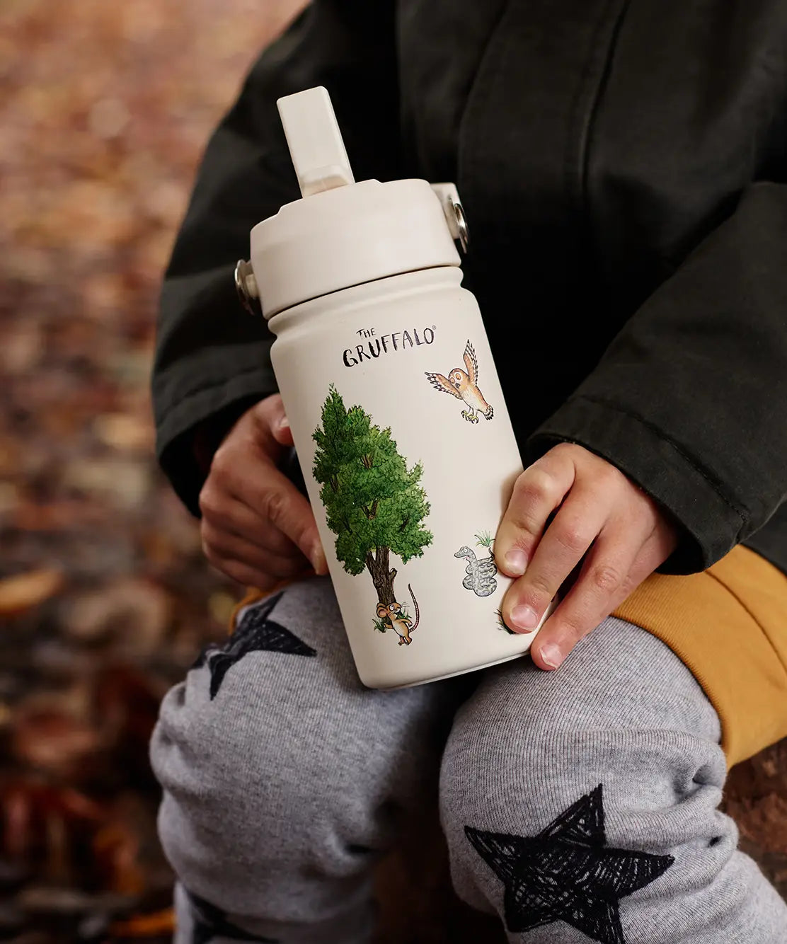 Child sitting on a tree stump and holding a stainless steel cream One Green bottle water bottle with a Gruffalo characters