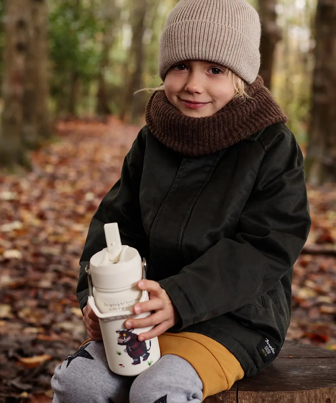 Child sitting on a tree stump and holding a One Green bottle stainless steel water bottle in cream with a Gruffalo characters