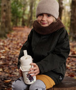 Child sitting on a tree stump and holding a One Green bottle stainless steel water bottle in cream with a Gruffalo characters