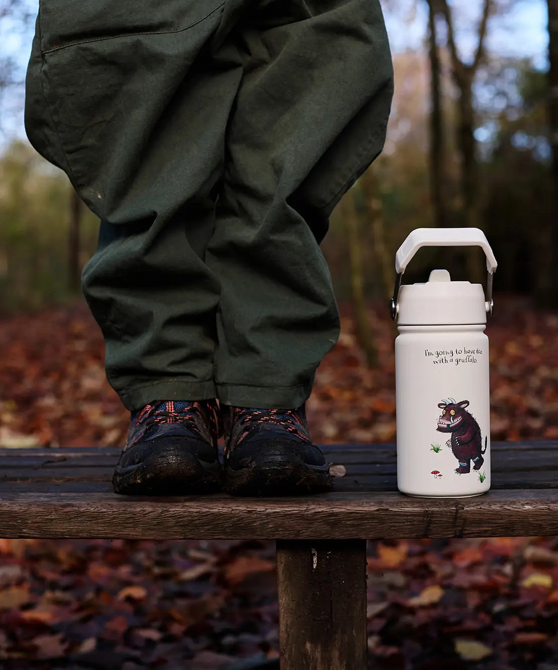 One Green Bottle stainless steel bottle in cream with a Gruffalo design standing on a wooden bench next to child's legs