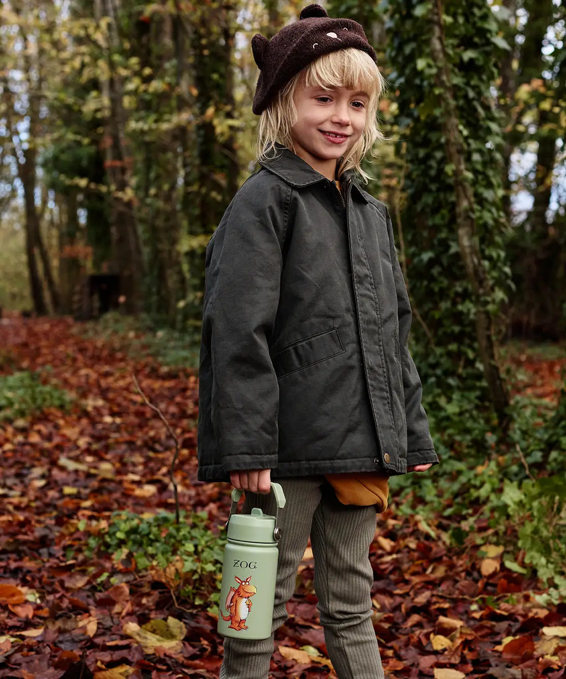 Child walking on Autumn leaves and holding a One Green Bottle stainless steel bottle in green with a Zog character