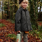 Child walking on Autumn leaves and holding a One Green Bottle stainless steel bottle in green with a Zog character