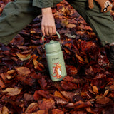 Child standing on Autumn leaves and holding a One Green Bottle stainless steel bottle in green with a Zog character