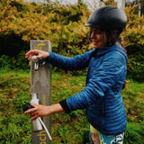 Woman refilling a stainless steel One Green Bottle 800ml water bottle with trees in the background