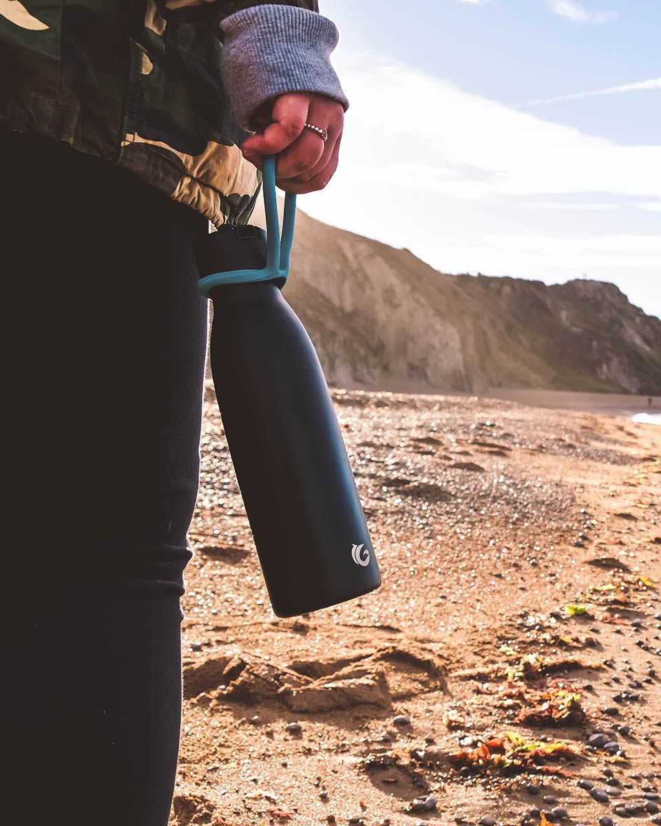 Close up of hand holding a One Green Bottle life collection canteen on a sunny beach 