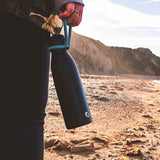 Close up of hand holding a One Green Bottle life collection canteen on a sunny beach 