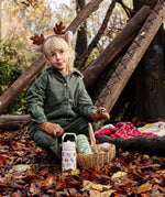 Child sitting next to a cream and green  One Green Bottle Zog collection bottles in the forest 