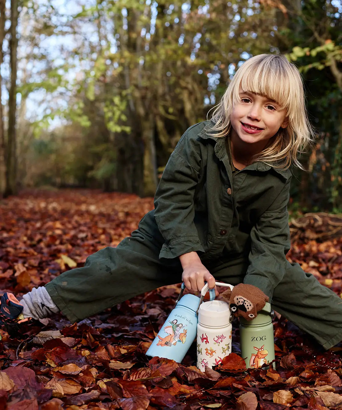 Child standing on autumn leaves and holding the One Green Bottle stainless steel Zog collection bottles