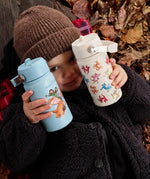 Child holding a blue and cream One Green Bottle stainless steel water bottles showing different Zog characters