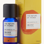 Orange pure essential oil in a blue glass bottle in front of a decorative yellow cardboard box.