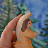 A orange coloured Ostheimer little angel held in an adult's hand to show scale. This wooden figure is part of a large range of expertly hand crafted, Waldorf inspired, wooden toys here at Babipur. 