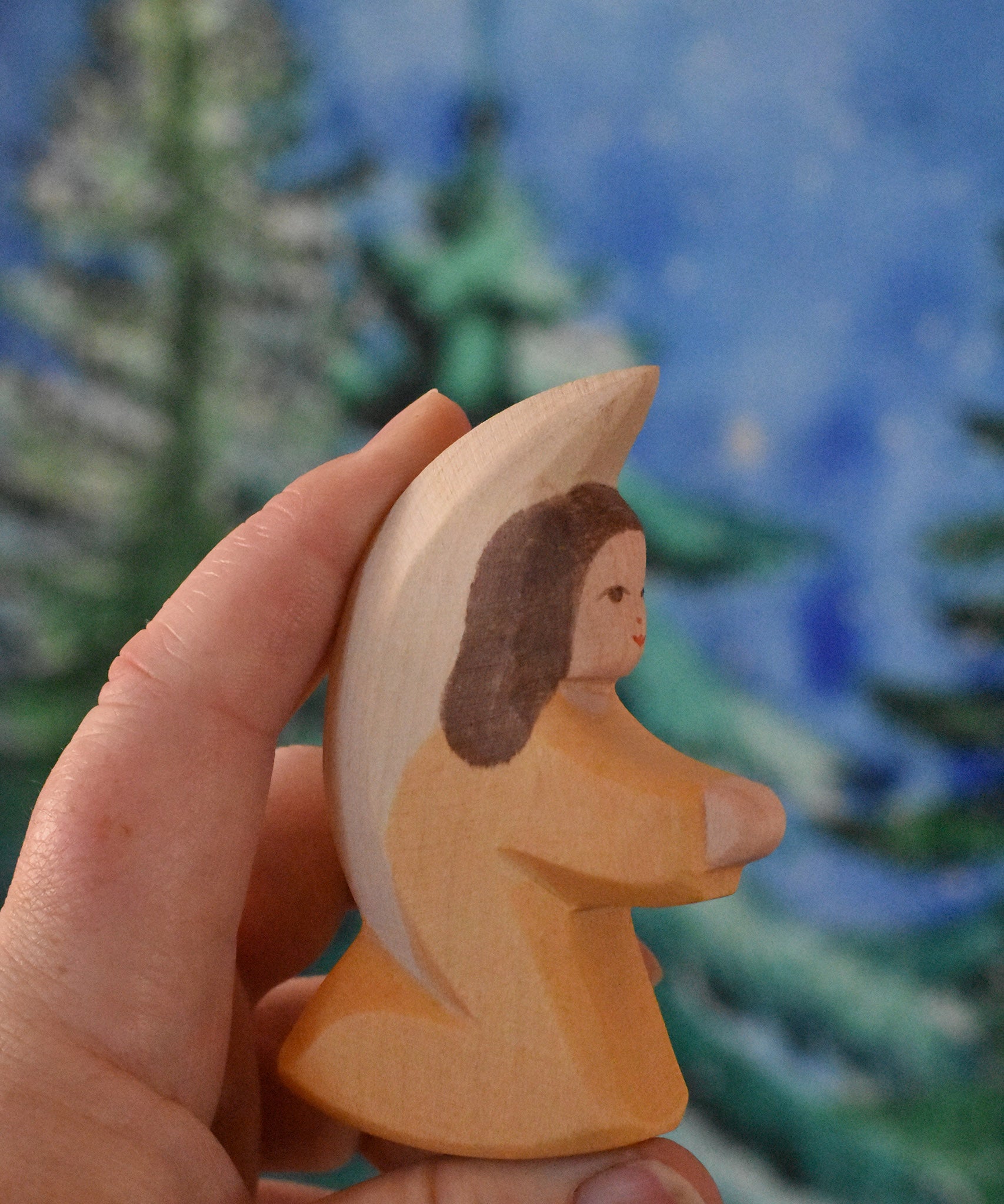 A orange coloured Ostheimer little angel held in an adult's hand to show scale. This wooden figure is part of a large range of expertly hand crafted, Waldorf inspired, wooden toys here at Babipur. 