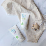 Green People Organic Babies unscented and lavender scented Baby Wash & Shampoo in 150ml tubes. The tubes have been placed on a linen coloured muslin cloth next to a wooden toy mouse. 