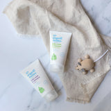 Green People Organic Babies unscented and lavender scented Baby Wash & Shampoo in 150ml tubes. The tubes have been placed on a linen coloured muslin cloth next to a wooden toy mouse. 