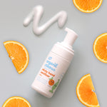 Organic Children sticky hands sanitiser on a light green background with some of teh product on the surface with slices of oranges. 