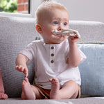 A child in a blue dress chewing on the Sophie The Giraffe So Pure Soft Teething Ring