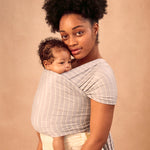 Ergobaby Aura Knit wrap in Grey Stripe. A parent happily carries their child on their front using the knit wrap