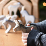 An Ostheimer Bremer wooden donkey figure in a child's hand. Other donkey figures can be seen blurred in teh background. Ostheimer's range of hand crafted, heirloom quality wooden toys are available to buy at Babipur. 