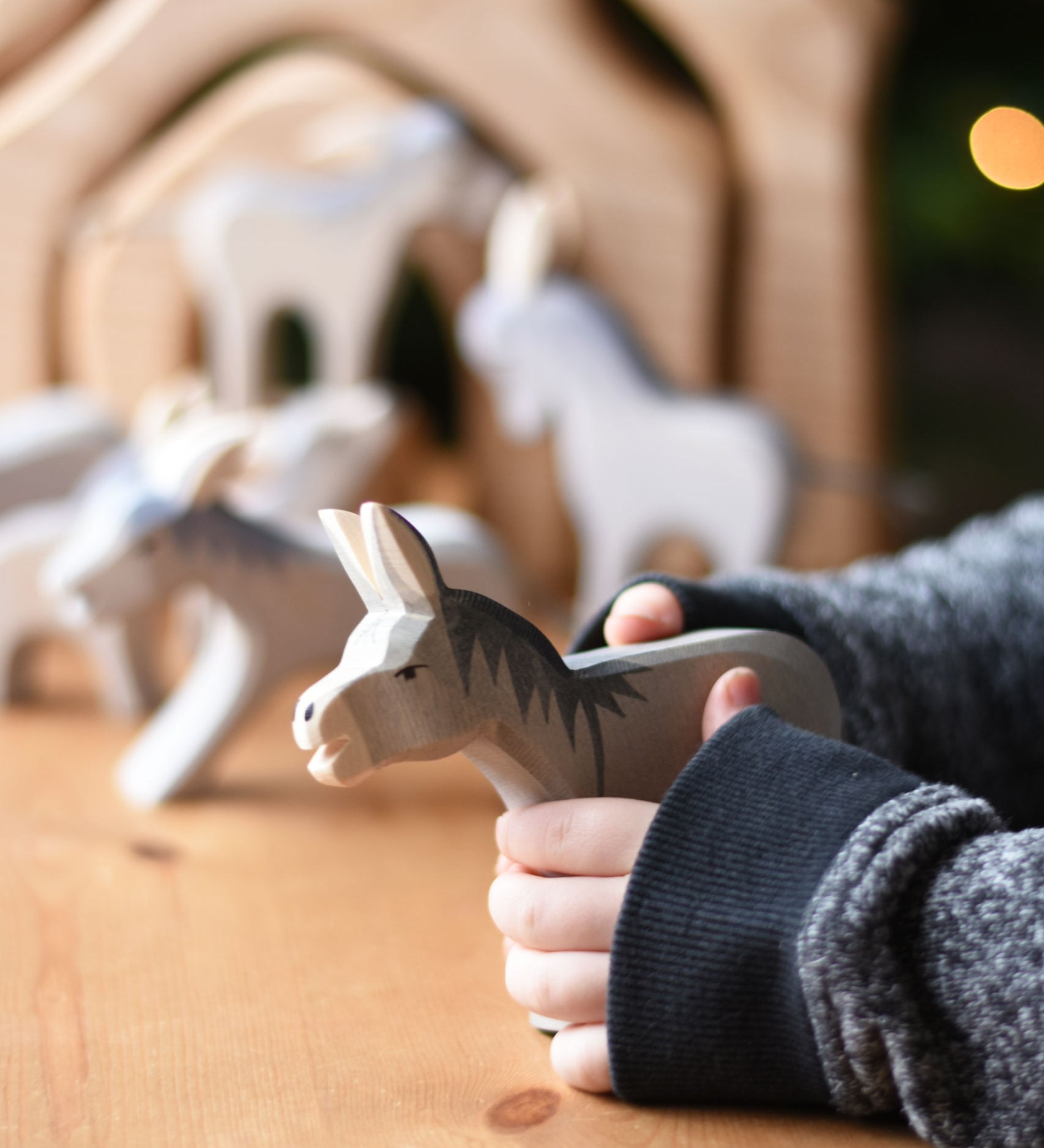 An Ostheimer Bremer wooden donkey figure in a child's hand. Other donkey figures can be seen blurred in teh background. Ostheimer's range of hand crafted, heirloom quality wooden toys are available to buy at Babipur. 