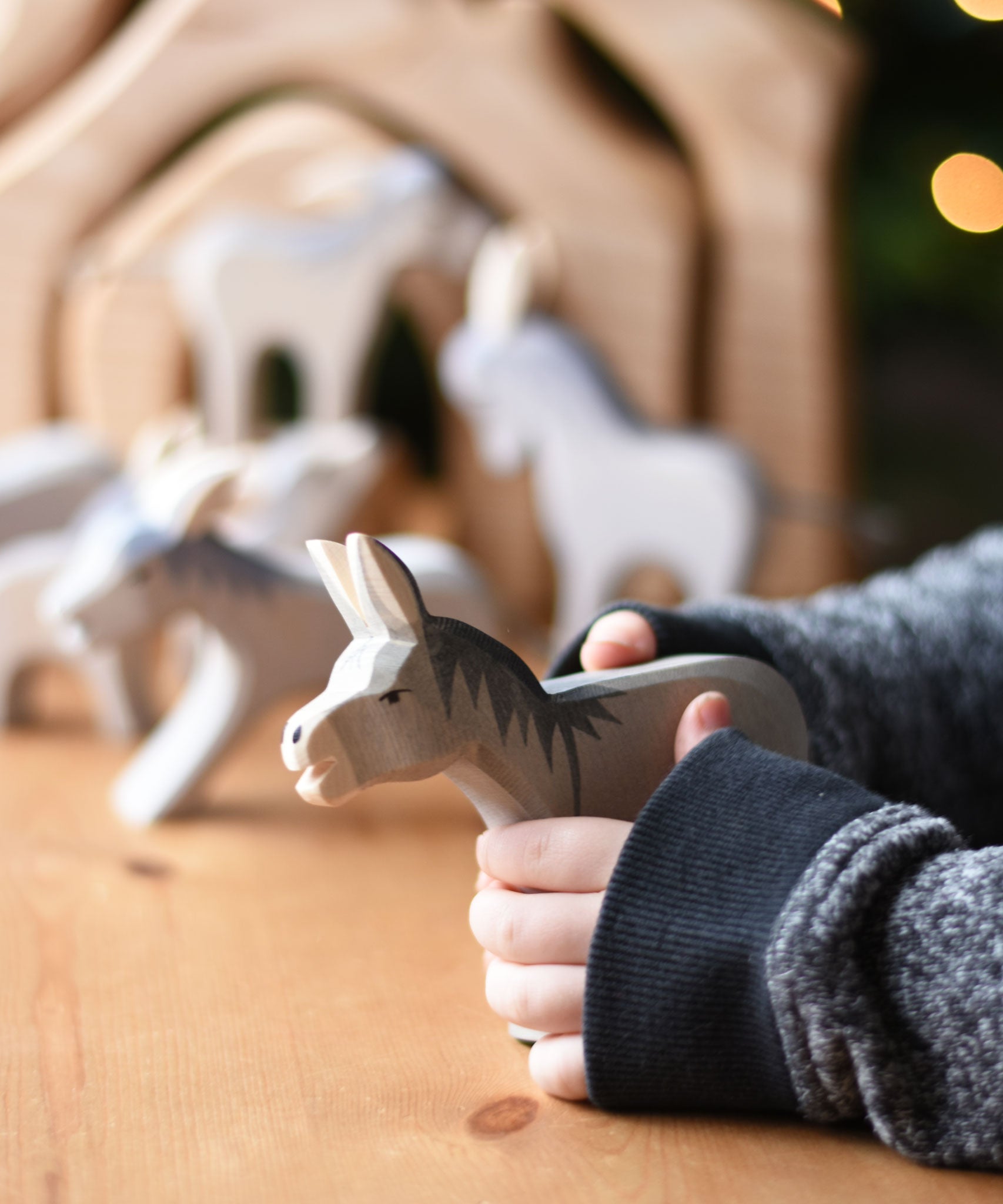 An Ostheimer Bremer wooden donkey figure in a child's hand. Other donkey figures can be seen blurred in teh background. Ostheimer's range of hand crafted, heirloom quality wooden toys are available to buy at Babipur. 