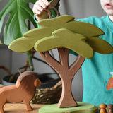 Ostheimer African tree wooden toy with support placed in a small world pay scene with lion figure A child is placing a standing baboon on top of the tree. 