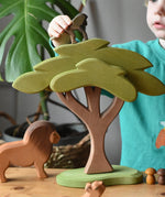 Ostheimer African tree wooden toy with support placed in a small world pay scene with lion figure A child is placing a standing baboon on top of the tree. 