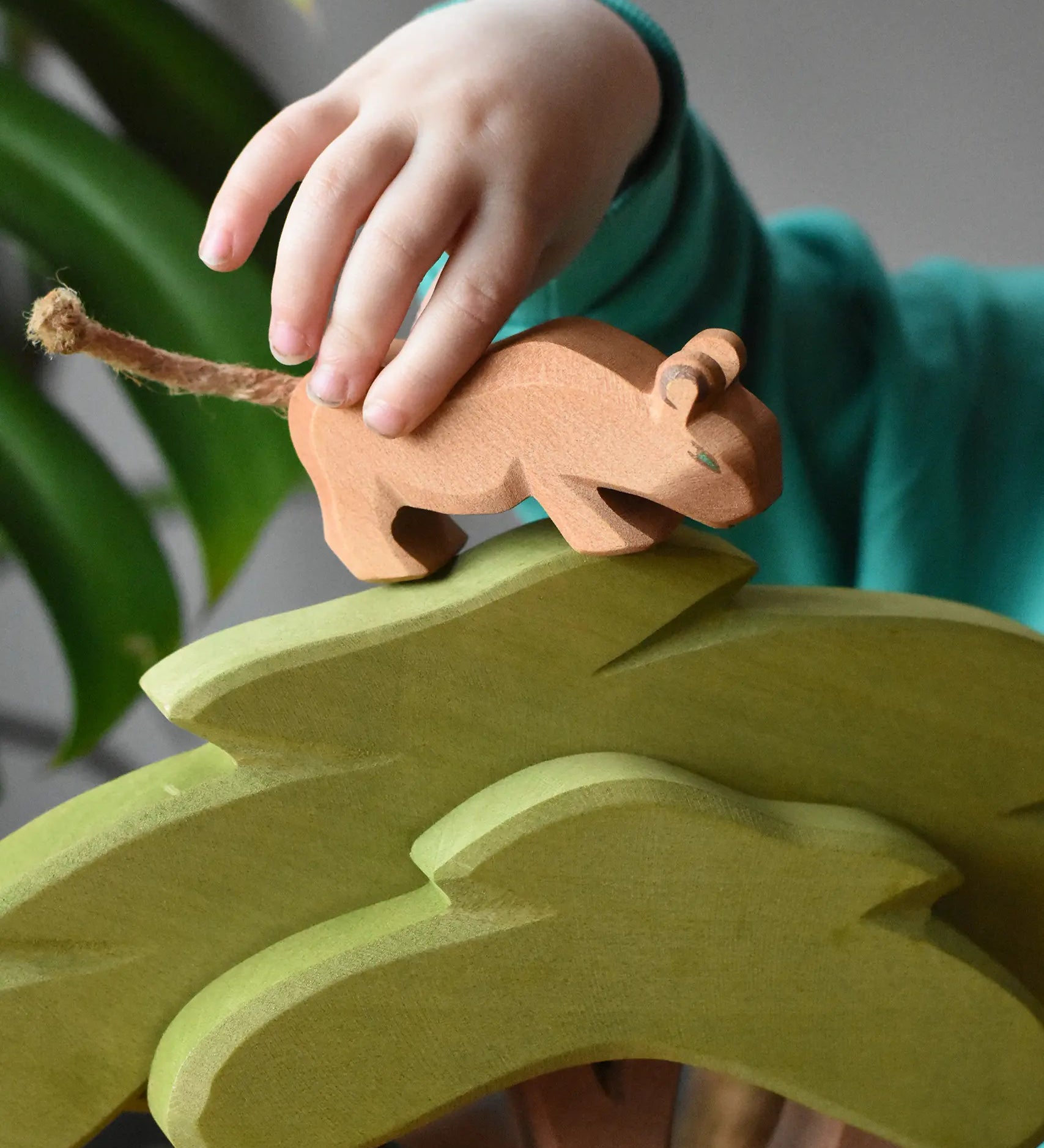 Child placing a small Ostheimer lion cub with head low on top of the African tree wooden toy figure. 