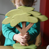 Ostheimer African tree wooden toy with support base held in a child's hands. 