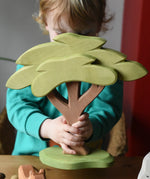 Ostheimer African tree wooden toy with support base held in a child's hands. 