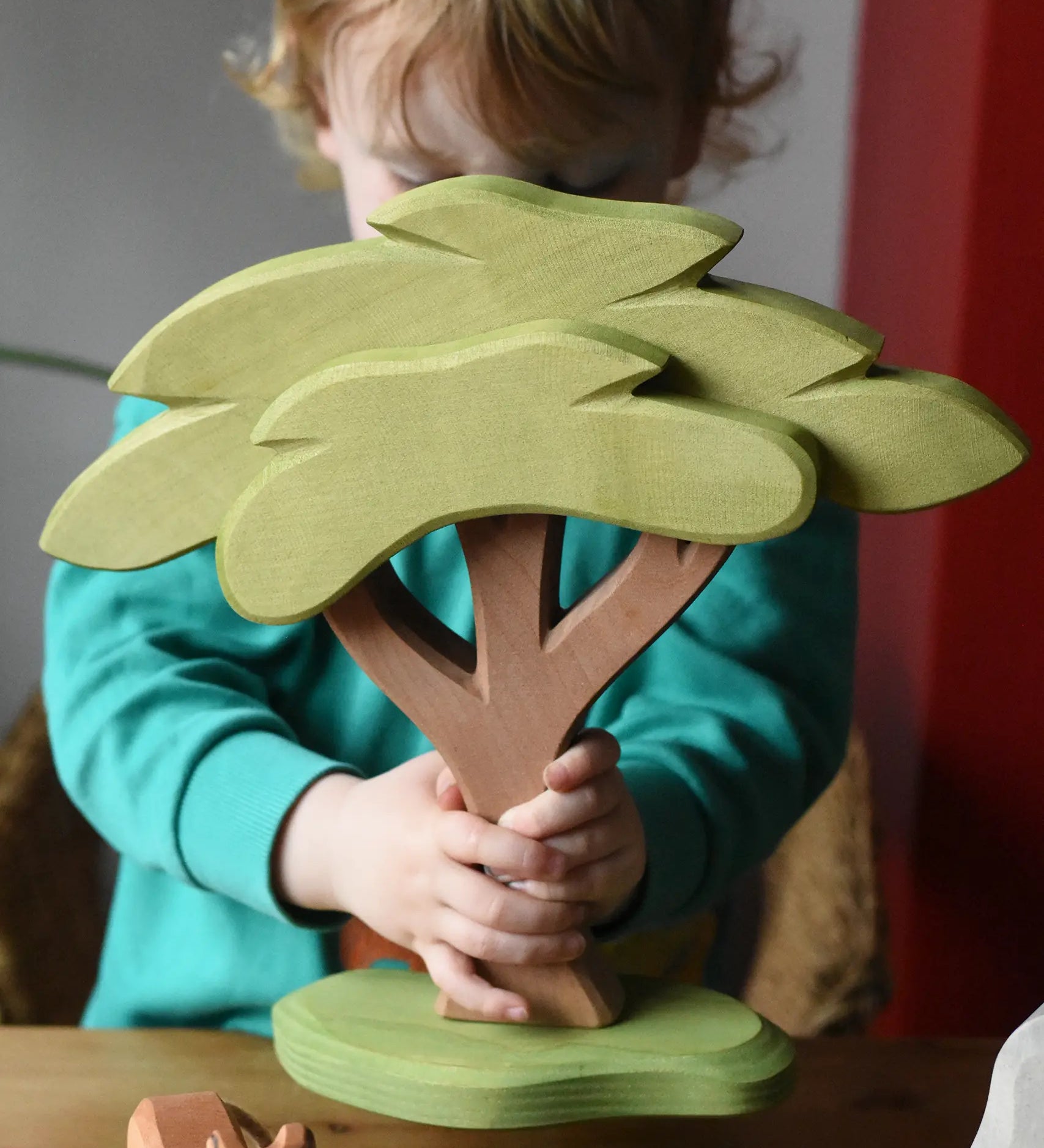 Ostheimer African tree wooden toy with support base held in a child's hands. 