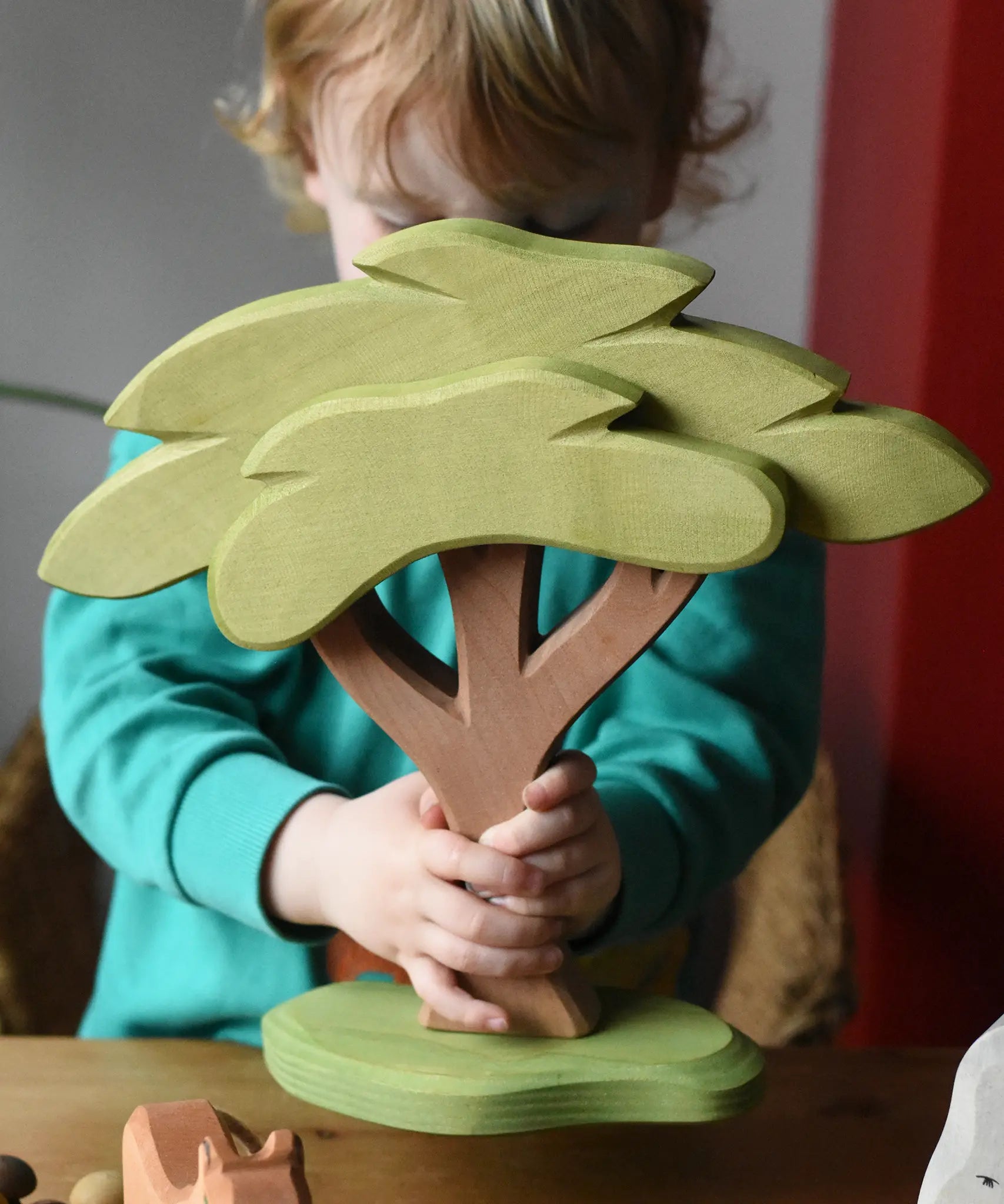 Ostheimer African tree wooden toy with support base held in a child's hands. 