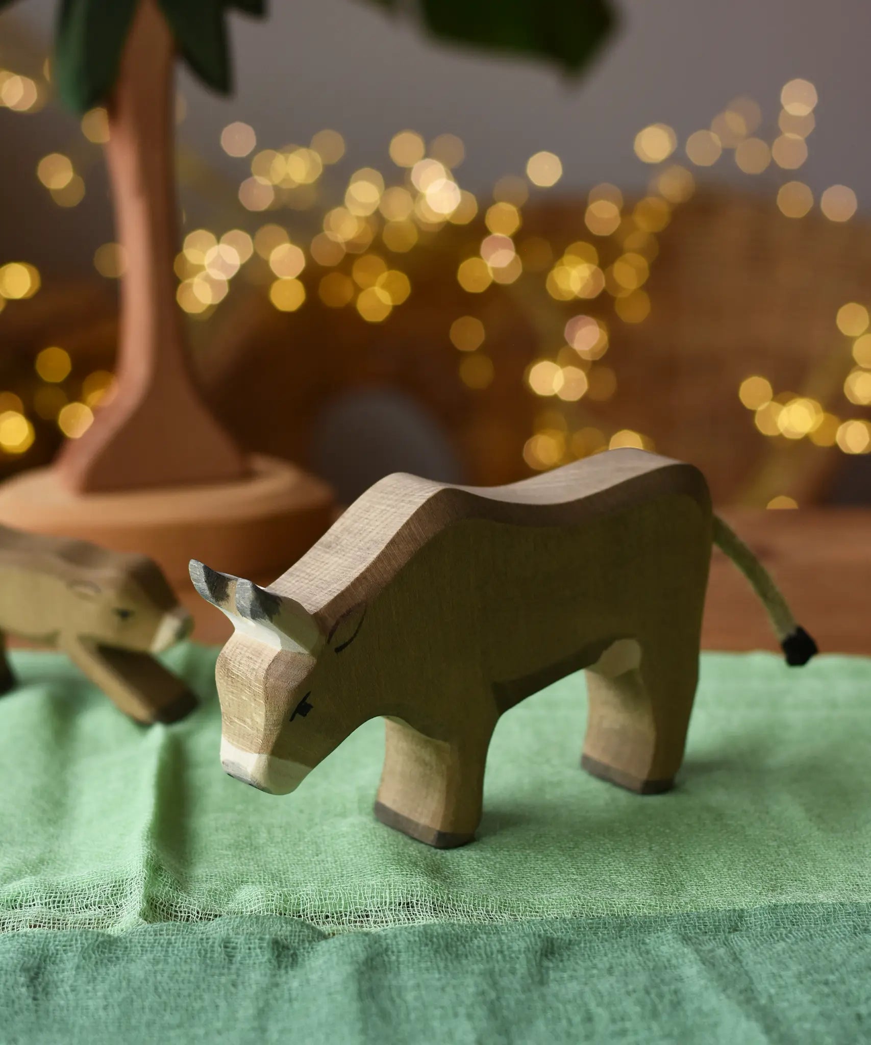 Ostheimer alp cow eating handmade wooden toy figure placed on green cotton play cloths. 