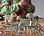 Ostheimer wooden baby animal figures a brown standing calf, running lamb and a black standing calf placed on a stool. A child can be seen in the background.