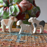 Ostheimer wooden baby animal figures a brown standing calf, running lamb and a black standing calf placed on a stool. A child can be seen in the background.