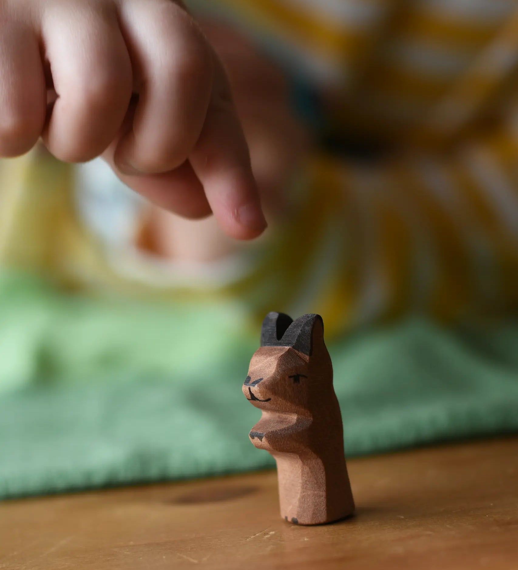 Ostheimer baby kangaroo handmade wooden toy figure placed on a wooden surface with a child's hand reaching for it.
