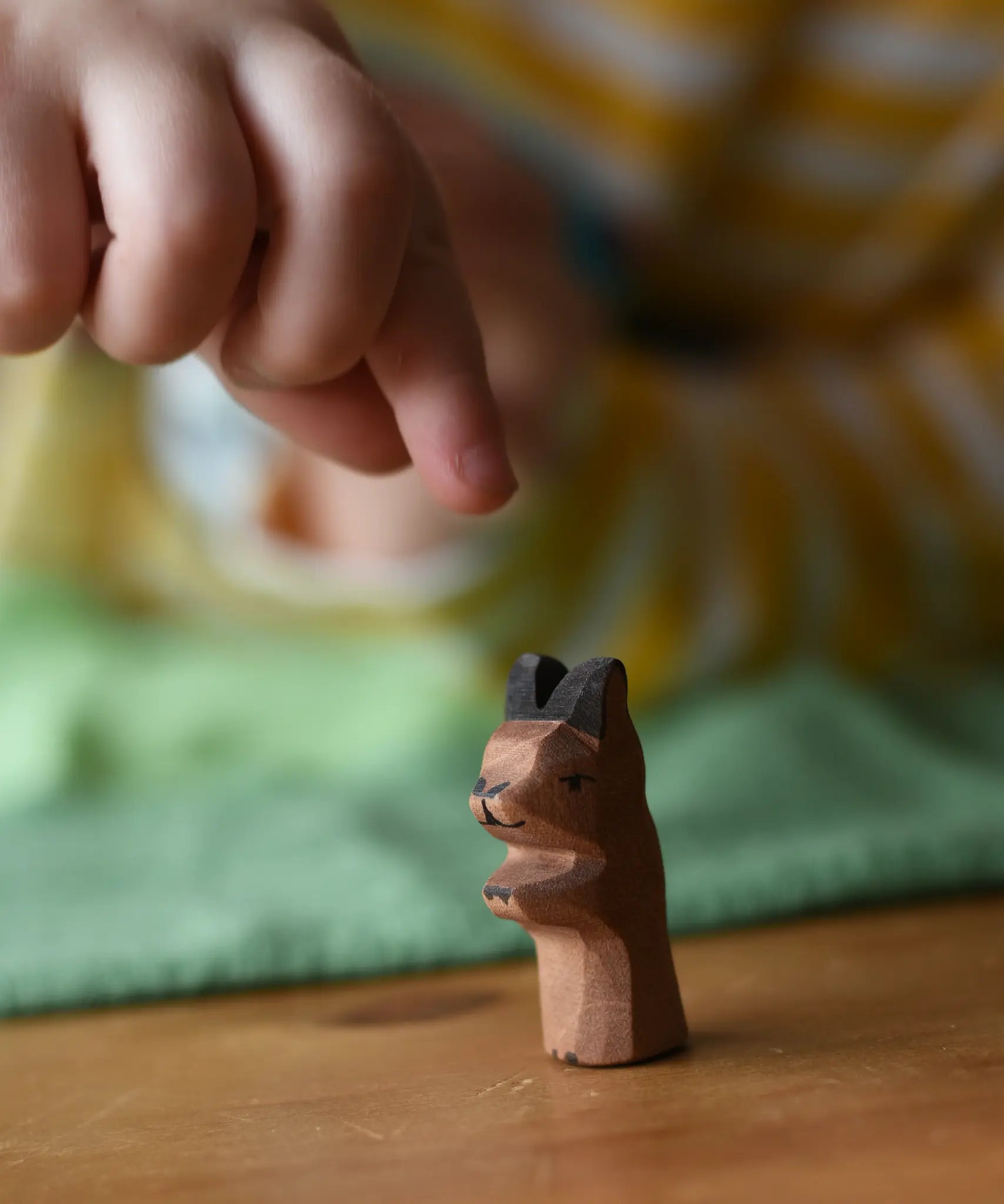 Ostheimer baby kangaroo handmade wooden toy figure placed on a wooden surface with a child's hand reaching for it.