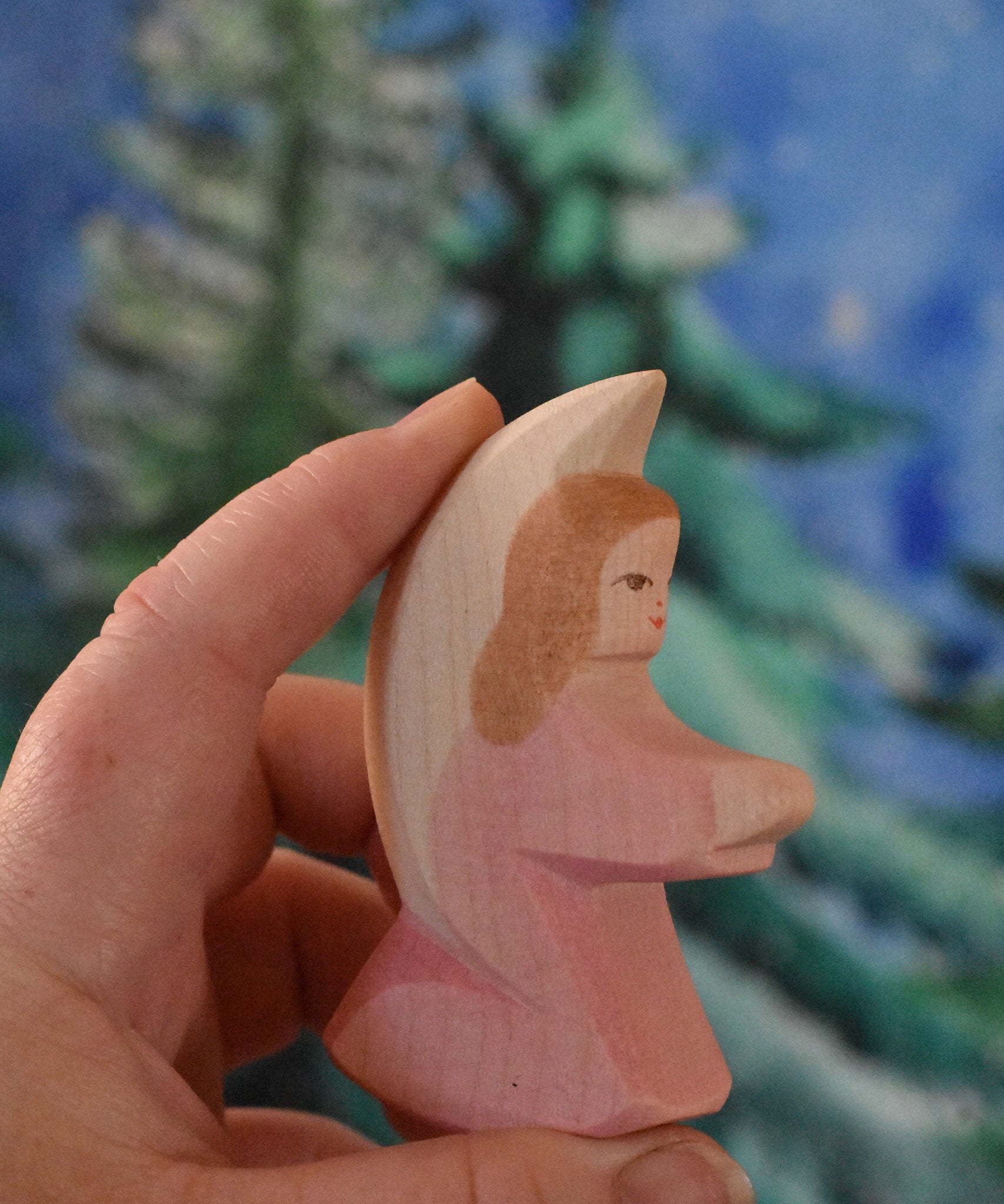 A pink coloured Ostheimer little angel held in an adult's hand to show scale. This wooden figure is part of a large range of expertly hand crafted, Waldorf inspired, wooden toys here at Babipur. 