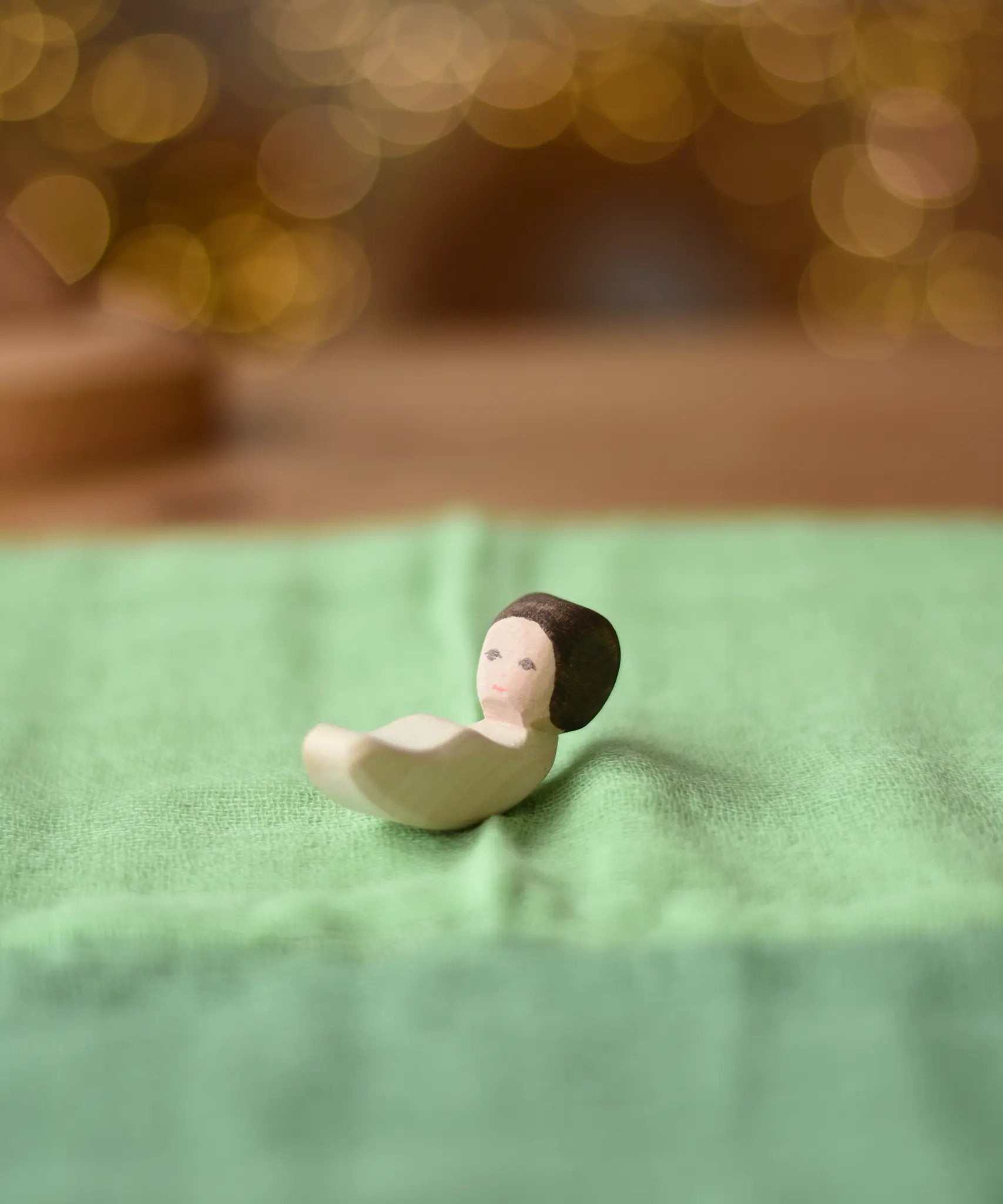 Ostherimer baby wooden toy figure placed on a light green cotton play cloth.