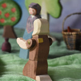A view of the back of the Ostheimer beggar wooden toy figure placed in a small world play scene. The figure has moveable arms and is wearing a raggedy brown outfit with holes and patches on. This wooden figure is part of a large range of expertly hand crafted, Waldorf inspired, wooden toys here at Babipur. 