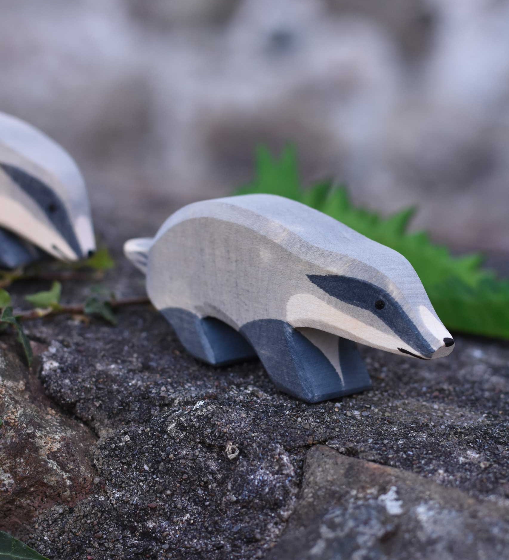 An Ostheimer wooden badger figure with straight head placed on a stone wall outdoors. Another badger figure can be seen in the background.