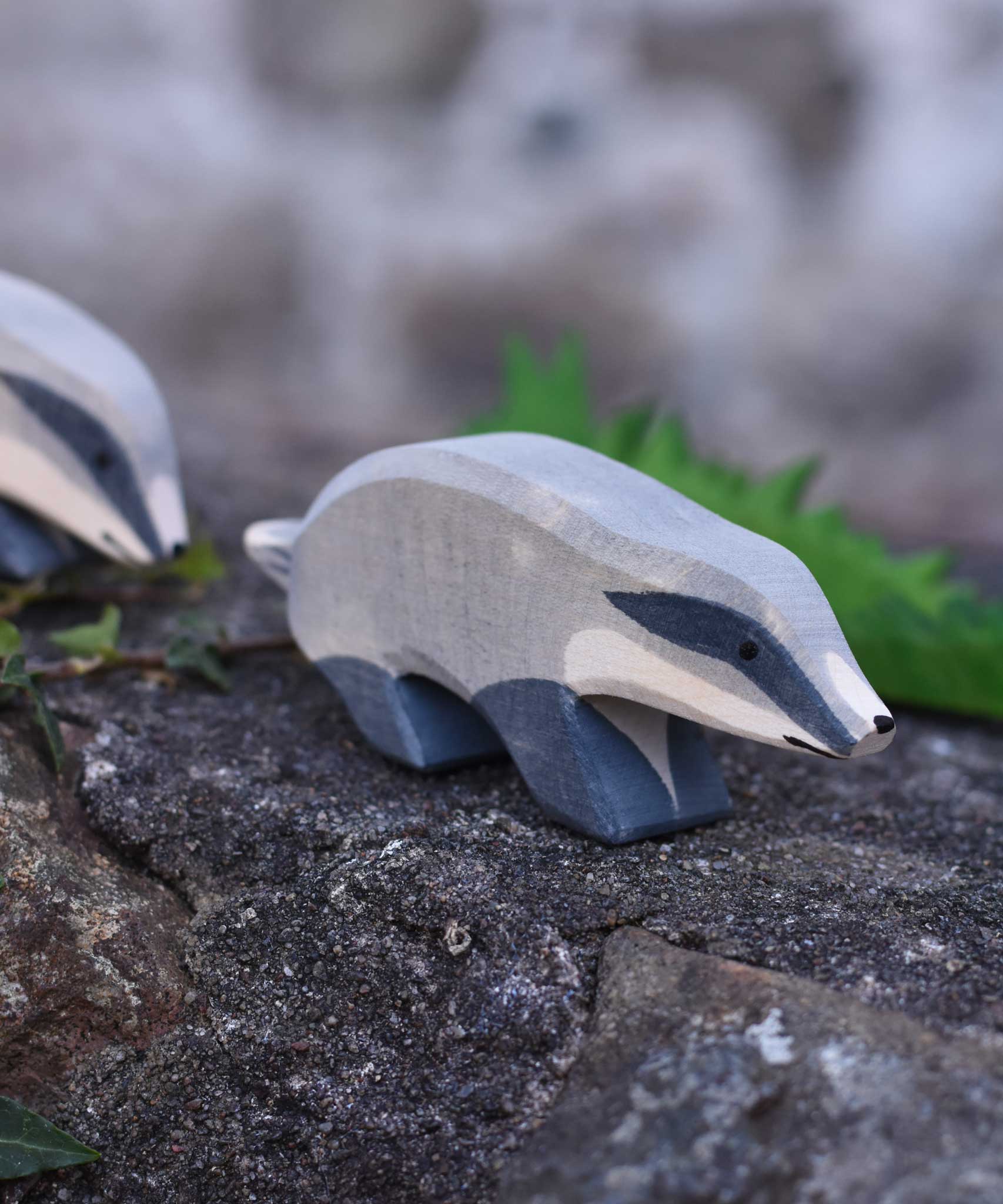An Ostheimer wooden badger figure with straight head placed on a stone wall outdoors. Another badger figure can be seen in the background.