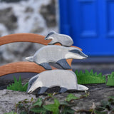 Three Ostheimer wooden badger figures tacked on top of each other on a stone wall outdoors. The badger at the bottom has it's head down the one in the middle  has it's had straight with the small badger placed on the top of the stack.